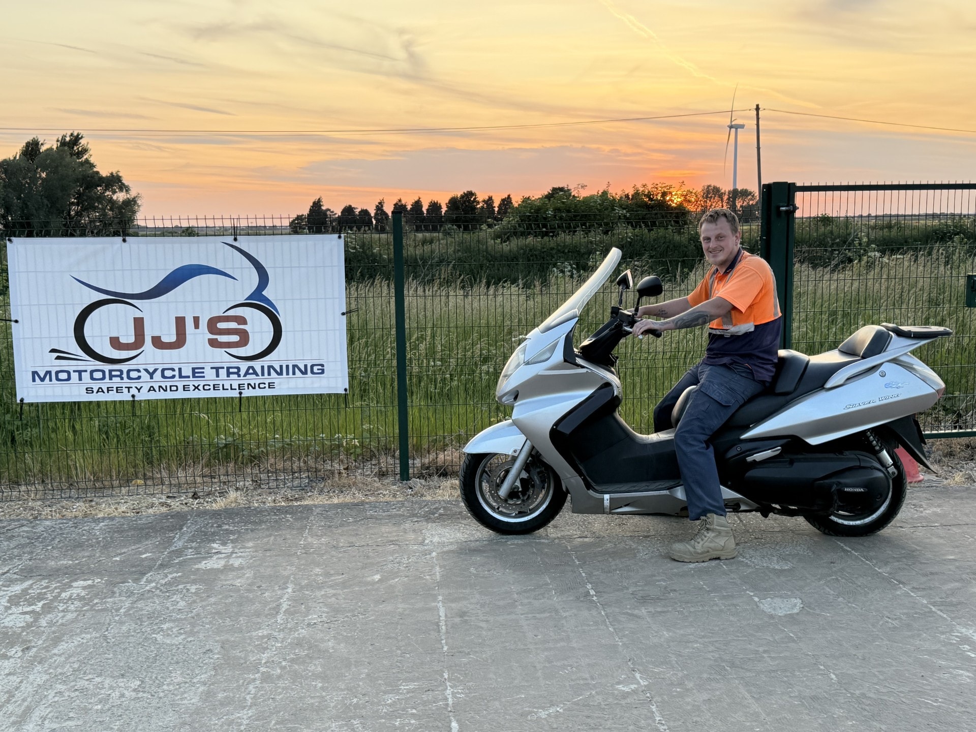 Instructor on scooter by JJ's sign at sunset