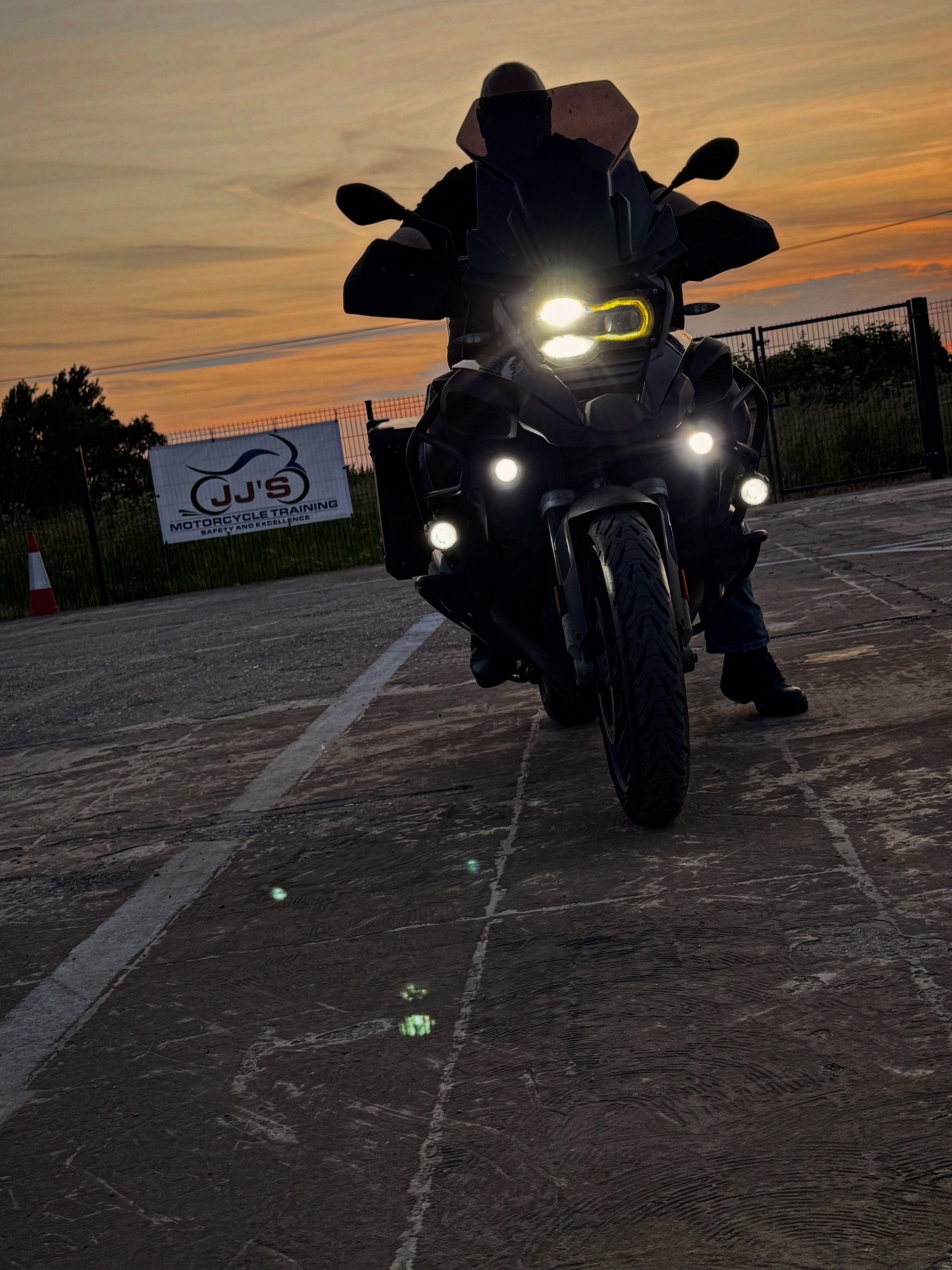 Motorcycle with headlights on at dusk by JJ's sign